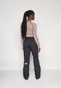 Langermet, tettsittende topp med stripete mønster i brune og beige farger, kombinert med svarte, løse bukser med logo på låret.