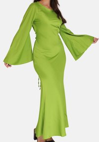 Lang grøn satin kjole med klokkeærmer, tætsiddende krop, udvidet nederdel og sidestropper. Glat tekstur, livlig farve, minimalistisk design.