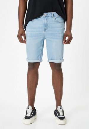 Lysblå denim shorts med optrukne bukseben, der har et klassisk fem-lomme design og falmede detaljer. Båret med sort-hvide sneakers.
