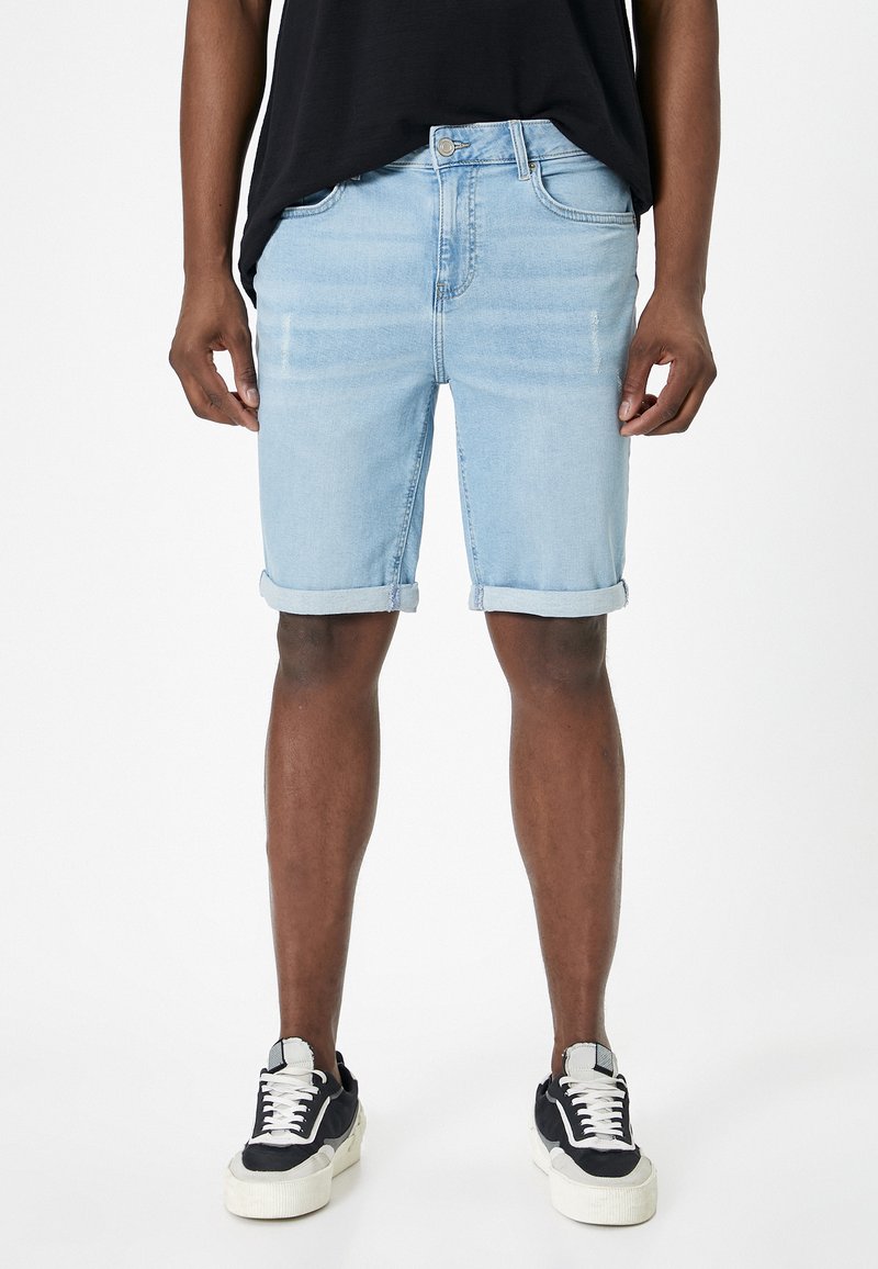 Lysblå denim shorts med optrukne bukseben, der har et klassisk fem-lomme design og falmede detaljer. Båret med sort-hvide sneakers.
