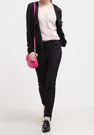 Mujer caminando con blazer negro, blusa rosa claro, pantalones negros, zapatos negros y llevando un pequeño bolso de hombro rosa brillante.