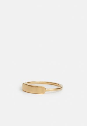 Anillo de oro simple con una parte superior plana y rectangular y una banda delgada y lisa descansando sobre una superficie blanca.
