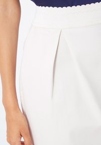 Falda blanca con una cinturilla ancha texturizada, que presenta un diseño plisado. La tela parece suave y ligera, adecuada para el uso casual.