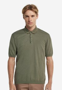 Olivgrön kortärmad polo skjorta i mjukt stickat tyg, med klassisk krage och plagg med tre knappar. Enkelt, strömlinjeformat design.