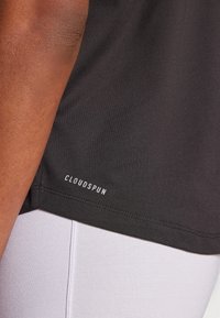 Černé sportovní tričko s hladkým povrchem, na spodním lemu s bílým logem "CLOUDSPUN". Detailní záběr odhaluje švy.