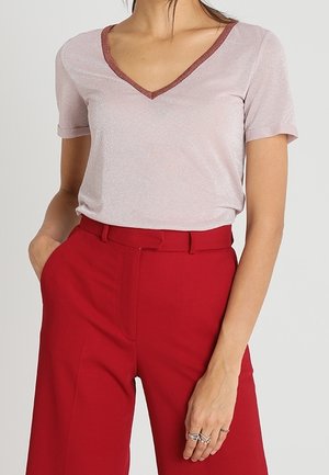 Maglietta a maniche corte rosa chiaro con scollo a V e dettagli in filo metallico, abbinata a pantaloni rossi a vita alta e gamba larga.