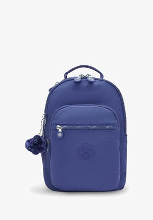 Sac à dos en nylon violet de forme arrondie, avec une poche zippée à l'avant, un écusson logo et un détail de breloque. Fermeture zippée double et poignée supérieure.