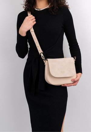 Borsa a tracolla beige realizzata in pelle liscia, con una patta arrotondata, dettagli in metallo dorato e una tracolla regolabile.