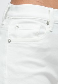 Witte spijkerbroeken van denim met een klassiek ontwerp met vijf zakken, metalen accenten en een gladde textuur met zichtbare stiksels langs de naden.