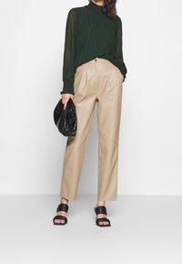 Blouse verte à motif avec col montant ; pantalon en cuir beige à jambes larges ; pochette noire texturée ; sandales noires à lanières plates.