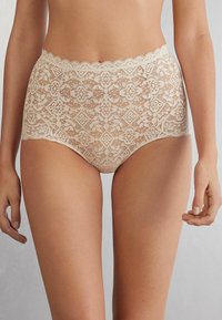 Beiga spetsiga högmidjade trosor med intrikata blommönster och diamantmönster, vågiga kanter och en genomskinlig textur.