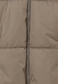 Giacca a vento beige con zipper centrale e sezioni trapuntate. Realizzata in materiale leggero e liscio con una texture morbida.