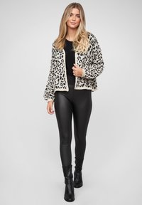 Leopardmønstret cardigan i beige og sort, strikket tekstur, åben front, lange ærmer. Sat sammen med sorte leggings og ankelstøvler.