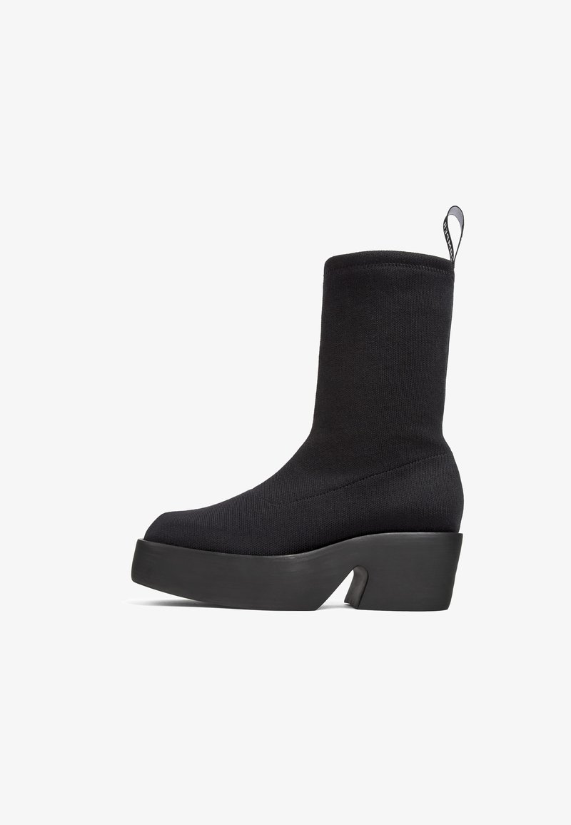 Botte chaussette noire mi-mollet avec semelle plateforme épaisse, talon bloc, bout arrondi et languette à l'arrière.