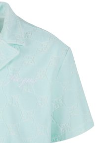 Camisa azul claro con un patrón floral en relieve, cuello estructurado y sutil texto bordado en blanco en la parte delantera. Textura de tela suave.