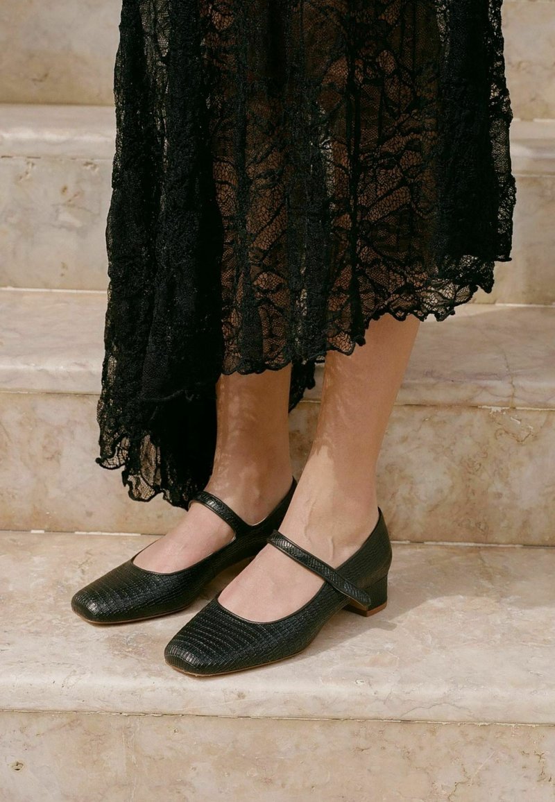 Scarpe in pelle nera con superficie texturizzata, dotate di punta quadrata e tacco a basso blocco, completate da una fascia decorativa sulla parte superiore del piede.