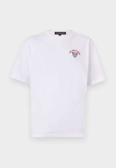 T-shirt blanc à manches courtes en coton avec un col rond, arborant un logo "LES BENJAMINS" brodé en rouge et noir ainsi qu'un détail graphique sur le devant.