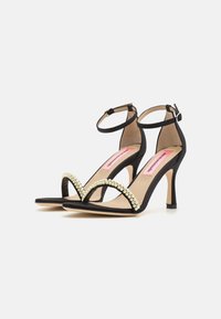 Black suede high-heeled sandals with a curved pearl-accented strap, adjustable ankle strap, and a pointed toe design.