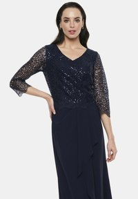 Granatowa sukienka z koronkowym górnym fragmentem z cekinami, dekoltem w kształcie litery V i rękawami o długości trzy czwarte; falująca spódnica z drapowanym detalem.