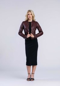 Veste en cuir bordeaux de type bomber avec une fermeture éclair à l'avant, au design ajusté et aux poignets côtelés, associée à une robe midi côtelée noire et à des sandales noires à brides.