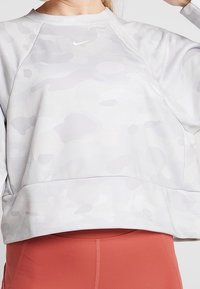 Felpa grigia chiara con un leggero motivo camouflage, scollo rotondo e orlo a costine. Presenta il logo Nike in bianco sul petto.
