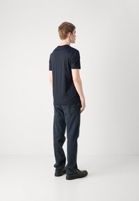 T-shirt a maniche corte blu navy con una texture liscia, abbinato a jeans scuri e scarpe nere. Design semplice, dettagli minimi, vista posteriore.