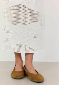 Fustă albă tricotată, cu un design din lucru deschis și modele florale. Asortată cu încălțăminte din suede maroniu. Textură subtilă și aspect ușor.