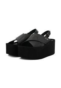 Sandali platform neri con cinghie incrociate e una fascia alla caviglia regolabile. Realizzati in pelle liscia con una suola spessa e strutturata.