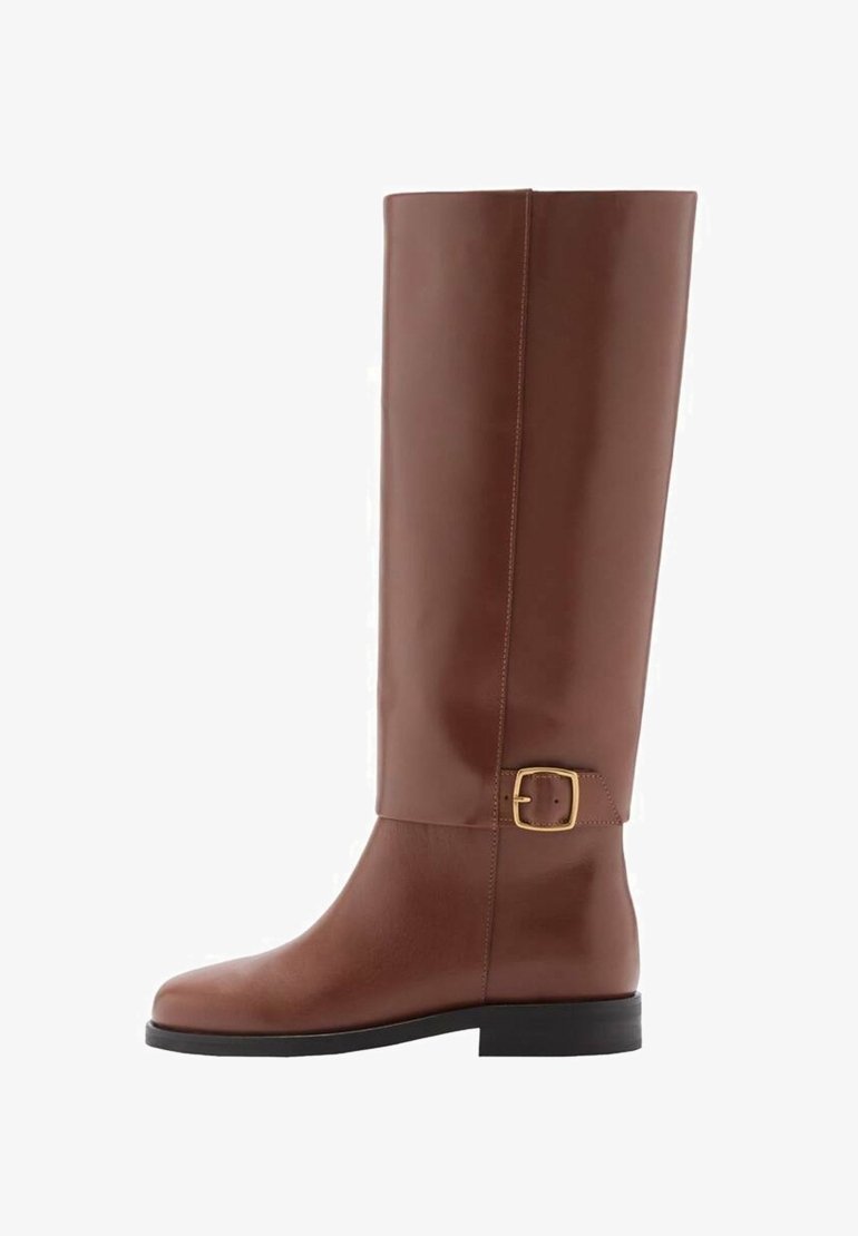 Botte haute en cuir brun avec une sangle à boucle dorée près de la cheville et un petit talon noir, vue de profil.