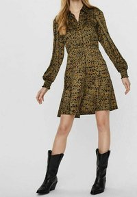 Långärmad grön klänning med blommönster, knäppning fram och utsvängd kjol; matchad med svarta cowboykängor.