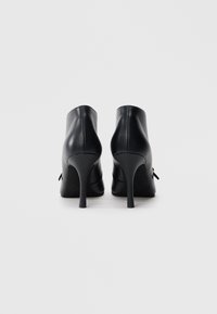 Μαύρα ψηλοτάκουνα μποτάκια αστραγάλου με λείο δερμάτινο φινίρισμα, που διαθέτουν κομψή σιλουέτα και στρογγυλεμένες μύτες, τονισμένα με μικρή μεταλλική λεπτομέρεια.