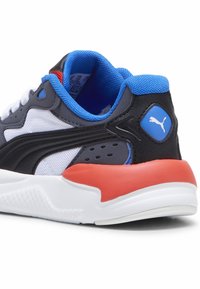 Scarpa sportiva in bianco e nero con rivestimento in rete blu, accentuazione arancione sul tallone, suola testurizzata e logo Puma in evidenza sul lato.