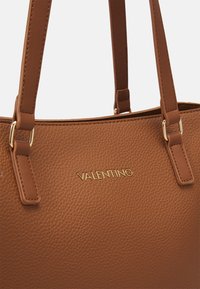 Hnědá texturovaná kůže taška na rameno se zlatým logem "Valentino", vybavená dvěma pevnými uchy a kovovými ozdobami.