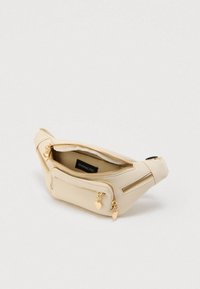 Μπεζ τσαντάκι μέσης με πολλαπλούς χρυσούς φερμουάρ σε σχήμα καρδιάς και ορατή ετικέτα μάρκας μέσα στο κύριο διαμέρισμα.