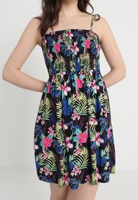 Blumiges Sommerkleid mit schwarzem Hintergrund, gerafftem Oberteil, verstellbaren Trägern und lebhaften tropischen Mustern in Pink, Blau und Grün.