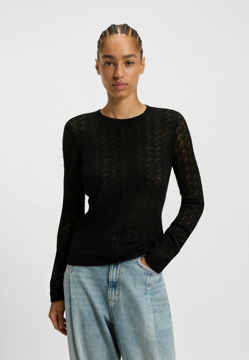 Pull noir à manches longues avec un motif zigzag texturé, silhouette ajustée et encolure ronde, associé à un jean clair ample.