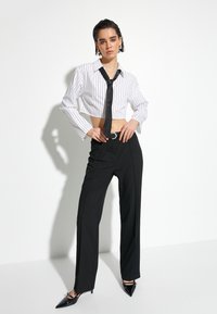 Vit och svart randig kortärmad skjorta med långa ärmar och svart slips, tillsammans med svarta vida byxor och spetsiga svarta klackar.