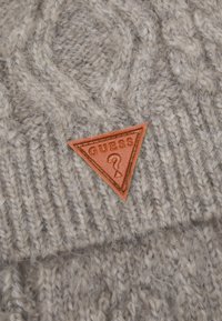 Tessuto a maglia grigio con un motivo testurizzato, dotato di una toppa triangolare in pelle arancione con la scritta "GUESS" in rilievo.