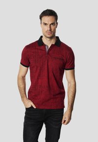 Punane polo särk tekstuurse mustriga, musta krae ja varrukaäärtega, kahe nööbiga plastriga ja vasakul rinnal tagasihoidliku logoga.