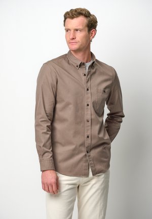 Camisa de manga larga, con botones, en un tejido de algodón de color marrón claro. Presenta un bolsillo en el pecho y botones negros con un diseño de cuello clásico.