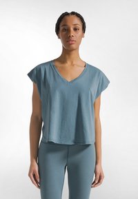 Lyseblå, kortærmet v-hals crop top lavet af blødt stof, med en afslappet pasform og en let buet kant.