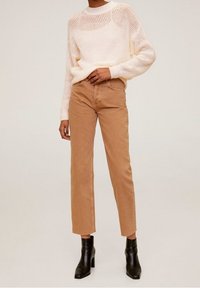 Pull en tricot crème à coupe ample et motif texturé, associé à un pantalon en velours côtelé marron clair à taille haute et des bottines noires.