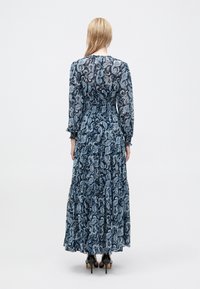 Μακριά φόρεμα σε ναυτικό μπλε με ανοιχτό μπλε σχέδιο paisley. Διαθέτει μακριά μανίκια, σφηκωτή μέση και πολυεπίπεδη φούστα. Υφή υφάσματος με γυαλάδα.