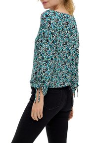 Bluse mit floralem Muster in Türkis, Schwarz und Weiß, mit langen Ärmeln. Hat geraffte Details und Bindebänder an den Handgelenken. Leichter Stoff.