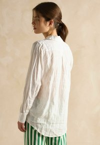 Biele plátenné tričko s voľným strihom, viditeľnou textúrou, dlhými rukávmi a zaobleným spodným okrajom, skombinované so zelenými a bielymi pásikavými nohavicami.