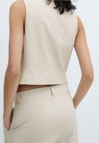Haut beige sans manches avec un design court et une texture lisse, associé à un pantalon ajusté coordonné doté d'une taille élégante.