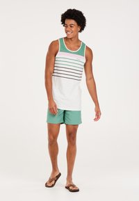 Mouwloos topje in het wit met groene, roze en bruine horizontale strepen; gecombineerd met mintgroene shorts en bruine slippers.