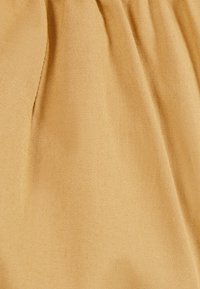 Beige fabric with a smooth, textured finish, featuring subtle lines and folds. Material appears lightweight and flexible.