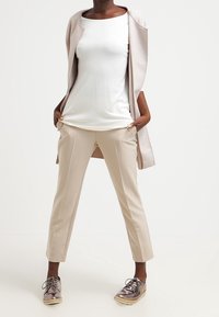 Pantaloni beige su misura con taglio dritto, abbinati a un top bianco aderente e a un cardigan aperto color marrone chiaro. Scarpe grigie lucide con lacci.