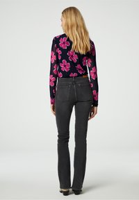 Langarmbloes met roze bloemen op een marineblauwe achtergrond, gecombineerd met hoge, donkere grijze flare jeans, bekeken van achter.
